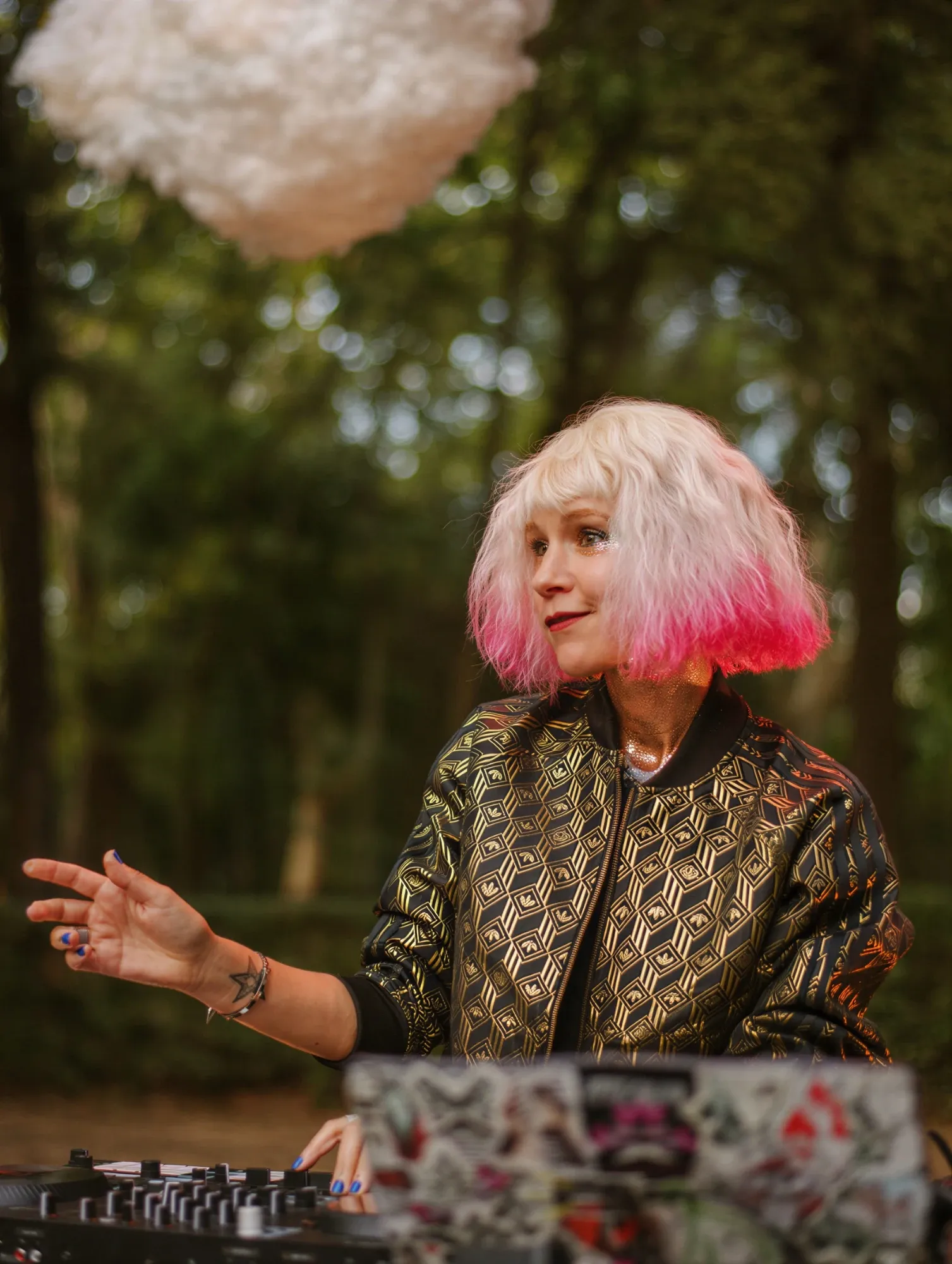 Emeraldia aux platines en plein air, cheveux blonds aux pointes roses, blouson doré, sous un nuage suspendu