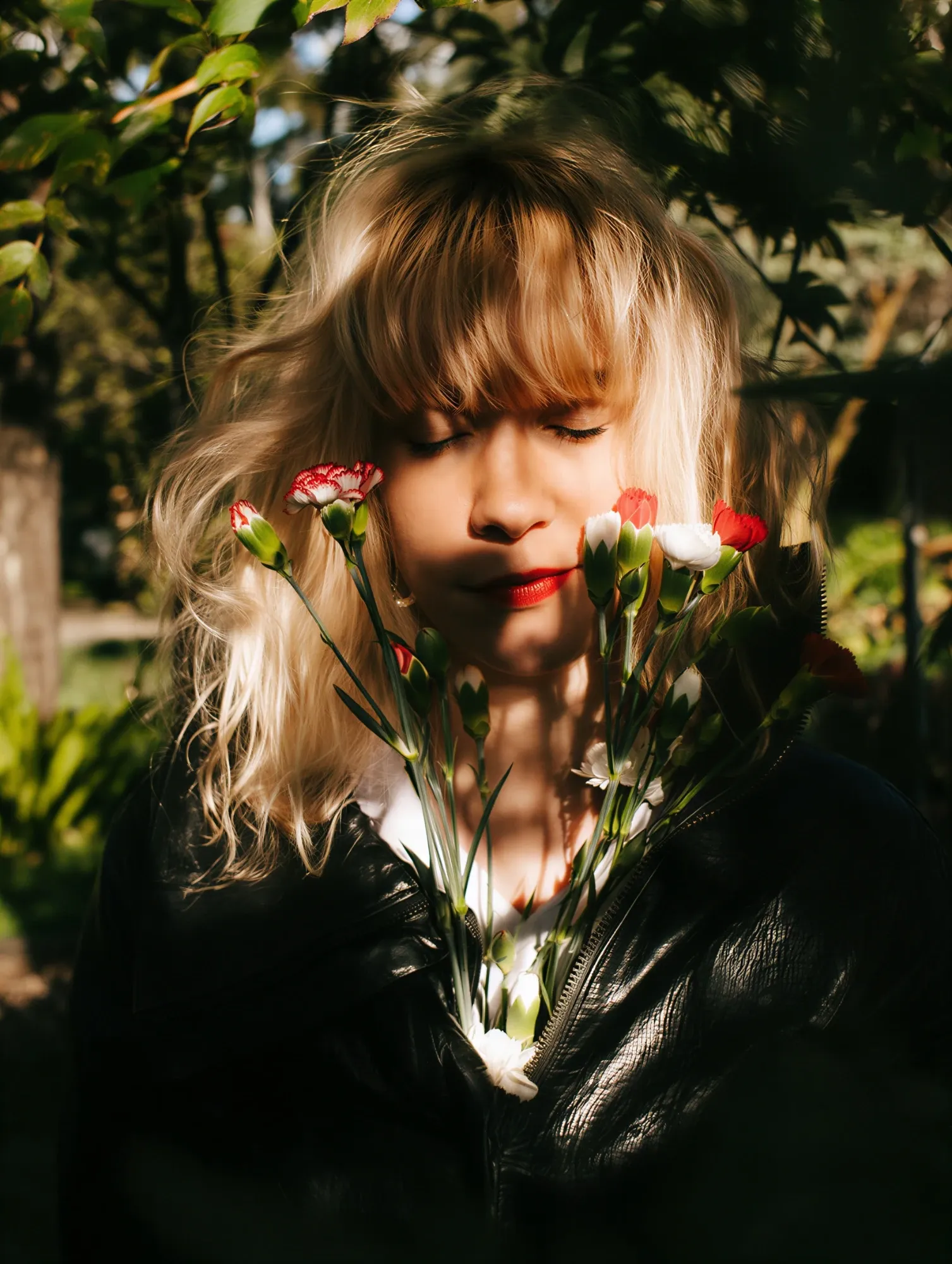 Emeraldia les yeux fermés, un bouquet d’œillets rouges et blancs, sous les feuilles
